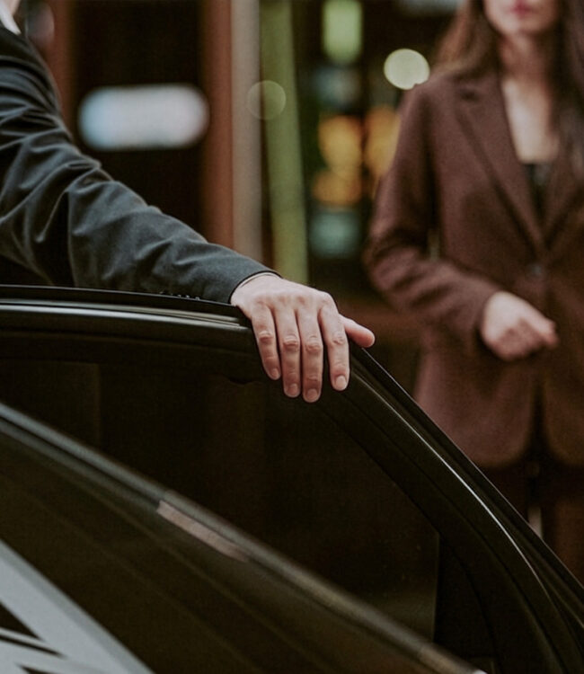 Services 1 Chauffeur services: Chauffeur holding the rear door of a black car open for a passenger